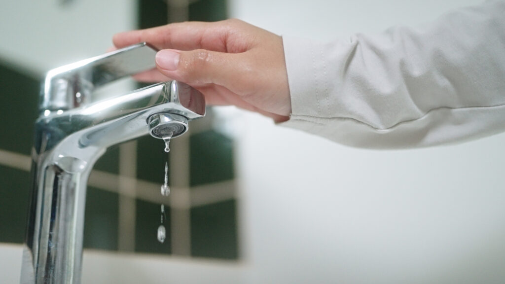 Close-up hand turning on or off faucet in bathroom.