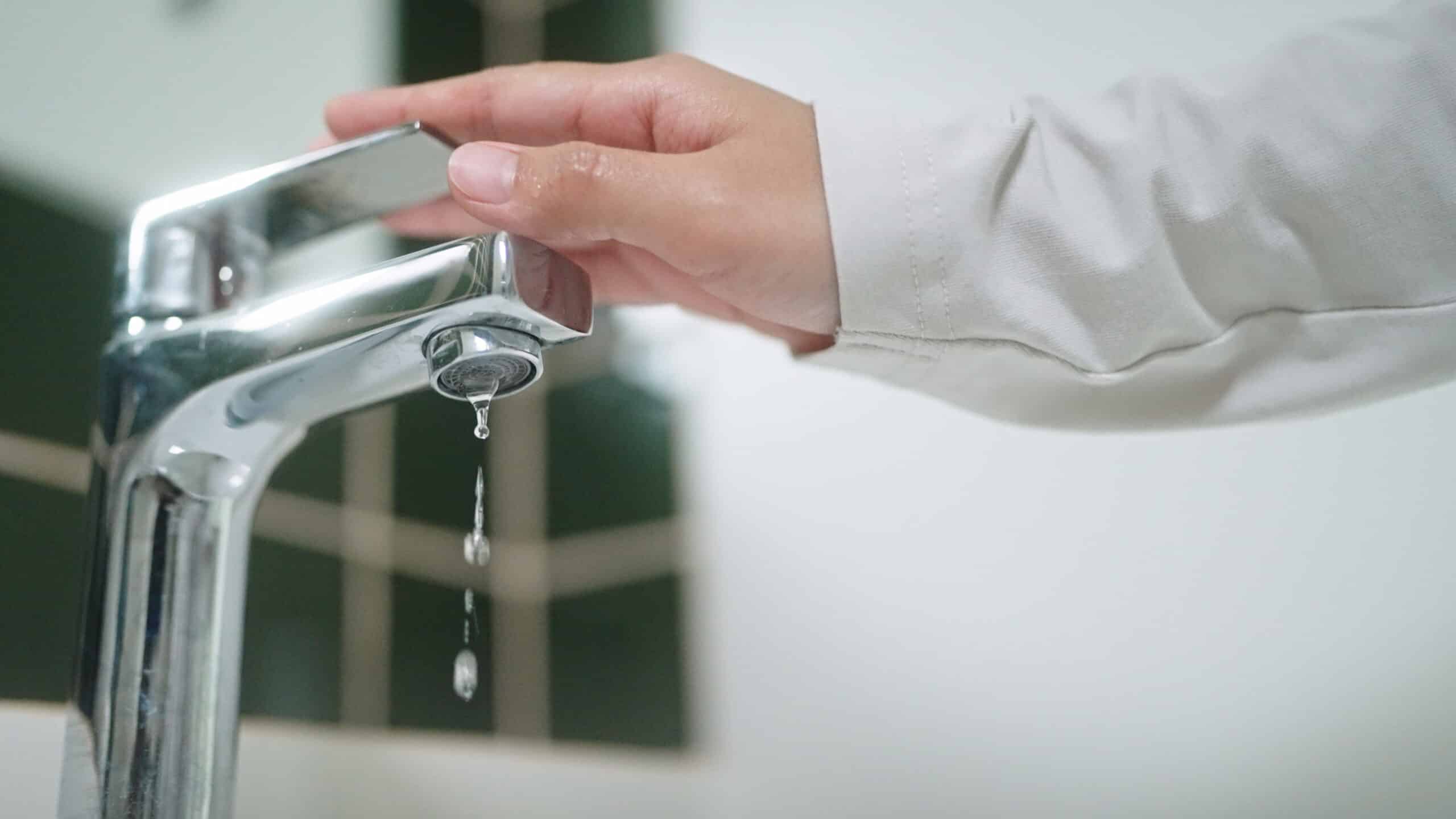 Close-up hand turning on or off faucet in bathroom.